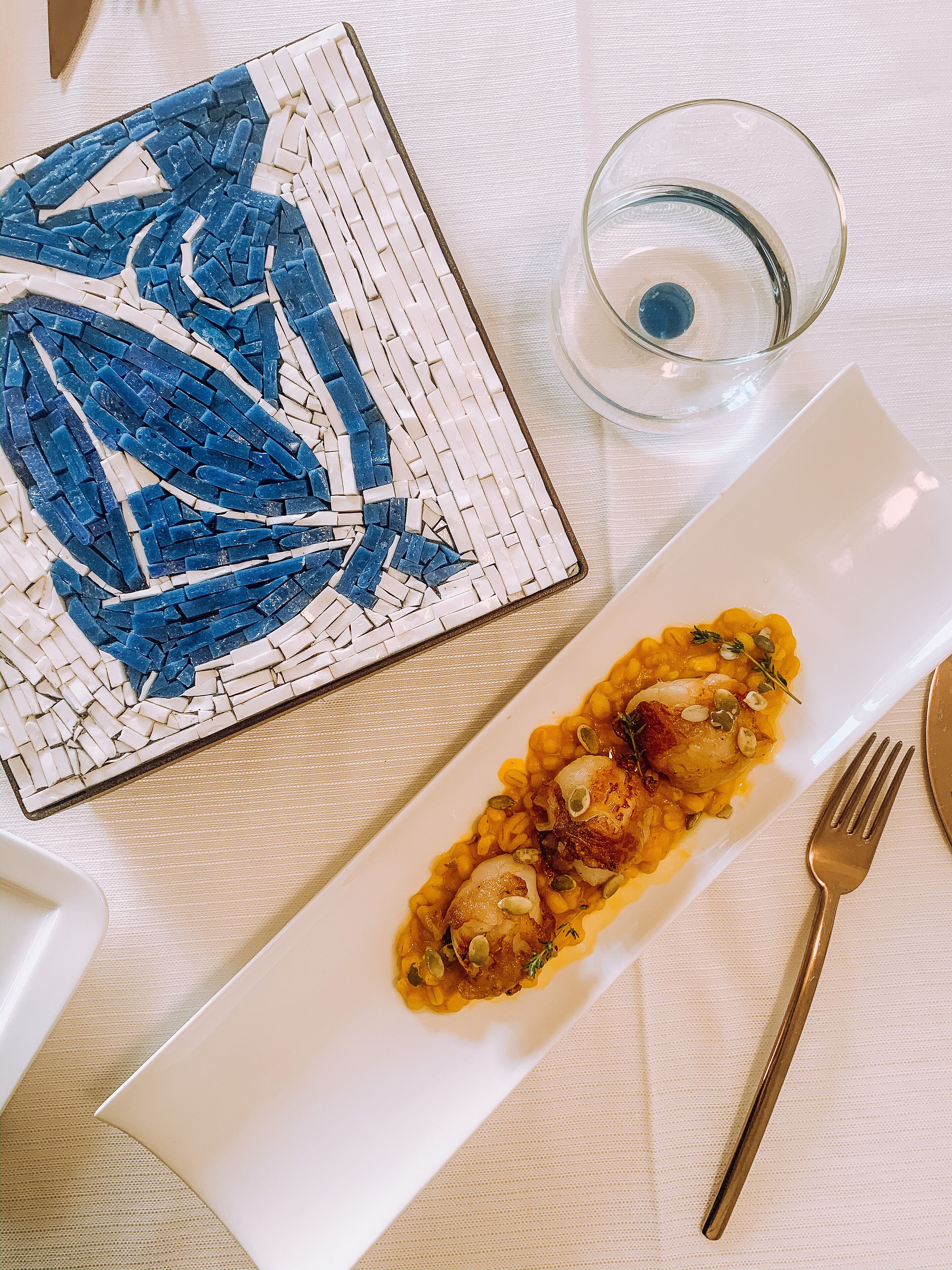 A dining table with a white plate of food, a glass of water, and a fork.
