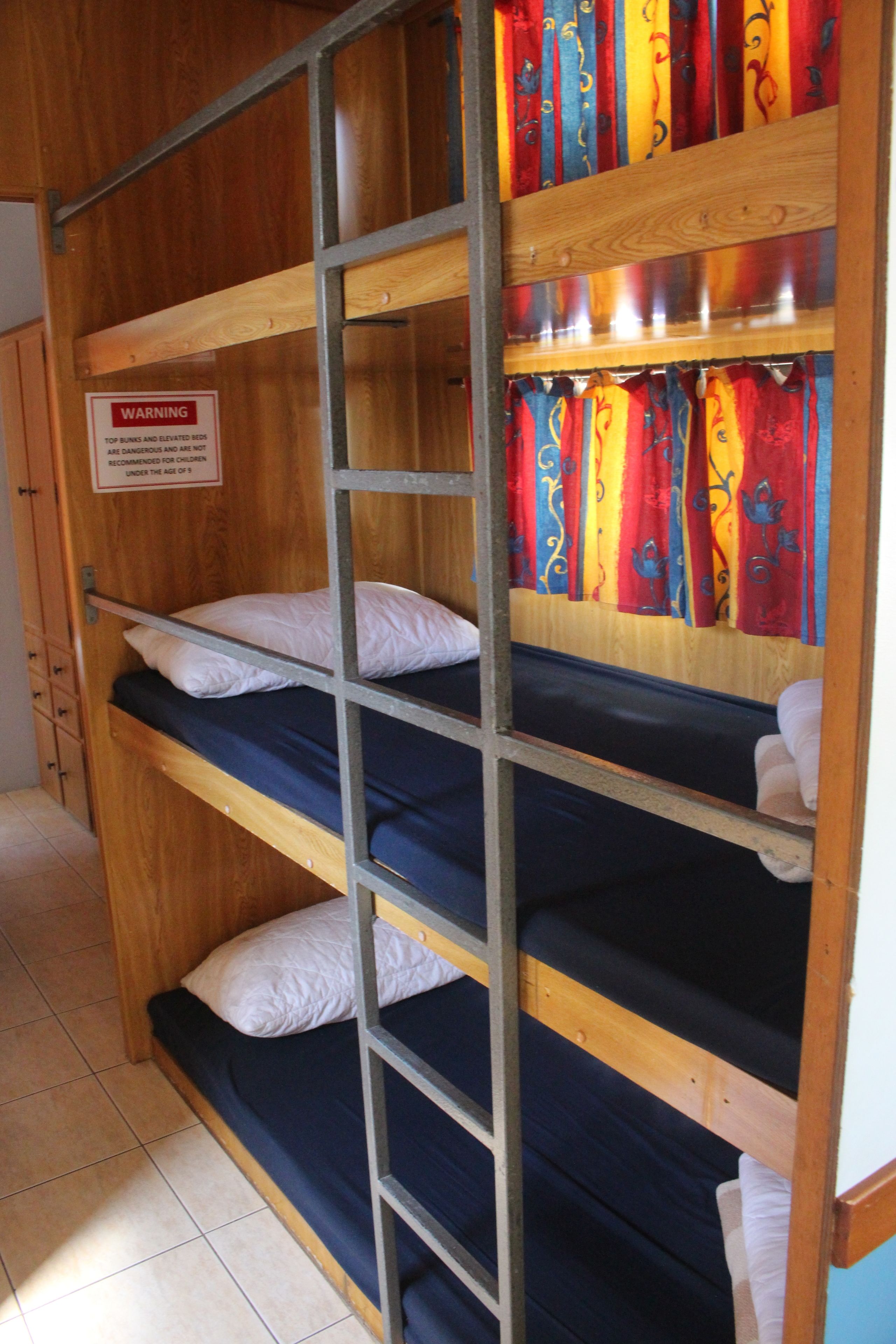 Een stapelbed met een waarschuwing, houten wanden en een betegelde vloer.