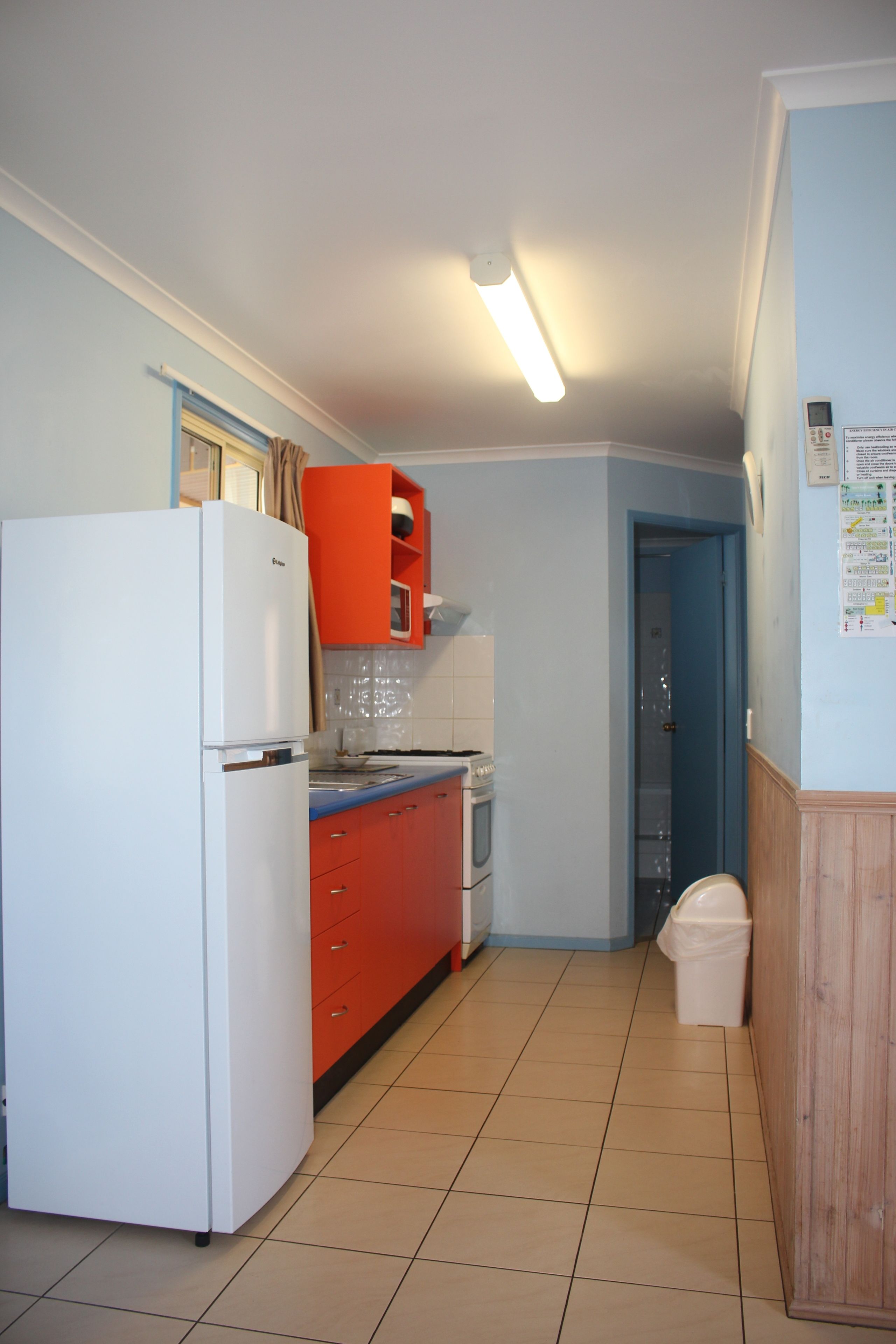 Cocina compacta con un refrigerador blanco, armarios rojos y un microondas en la encimera.