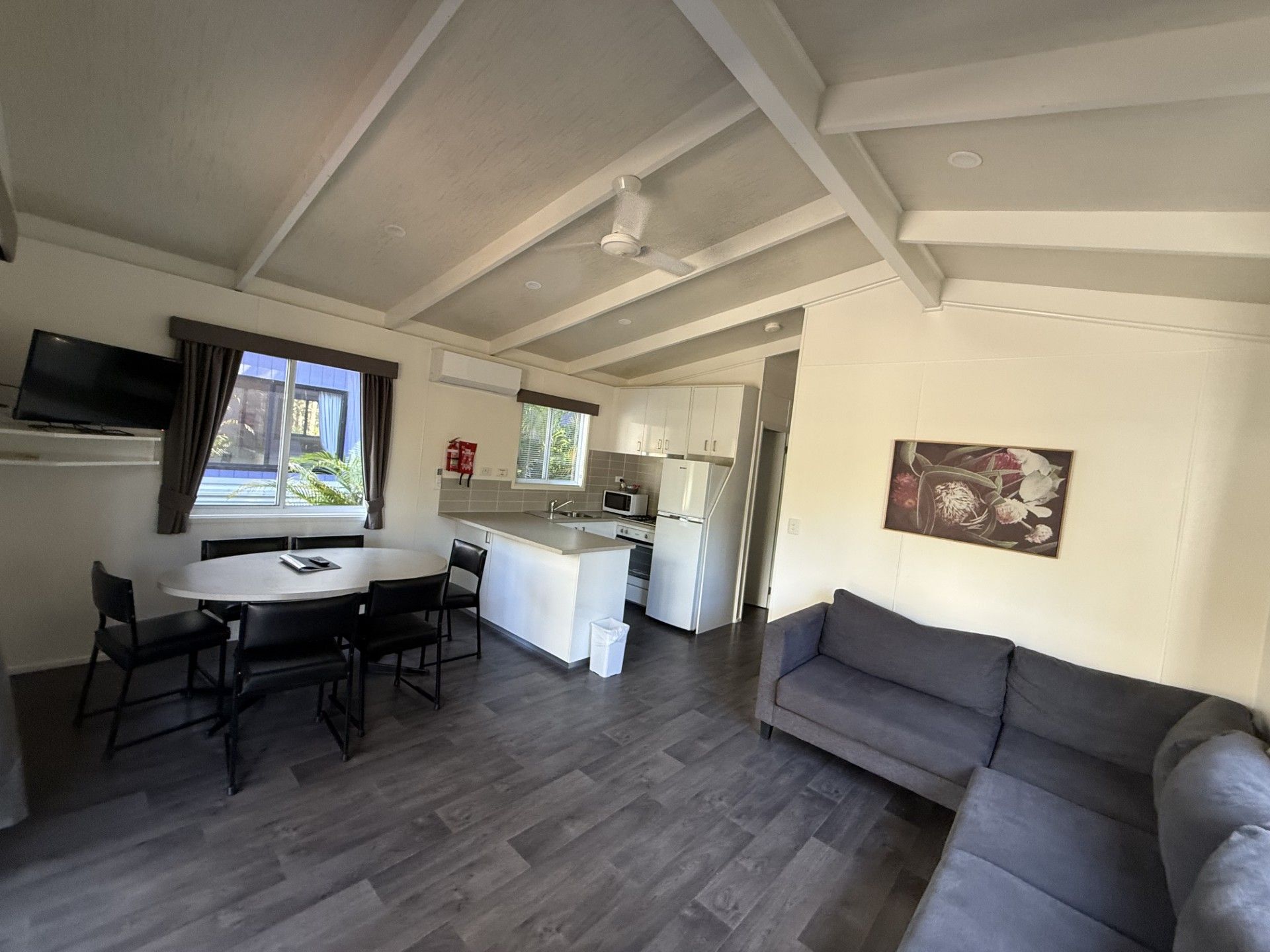 A modern living space with a dining area, kitchen, and a grey sofa.