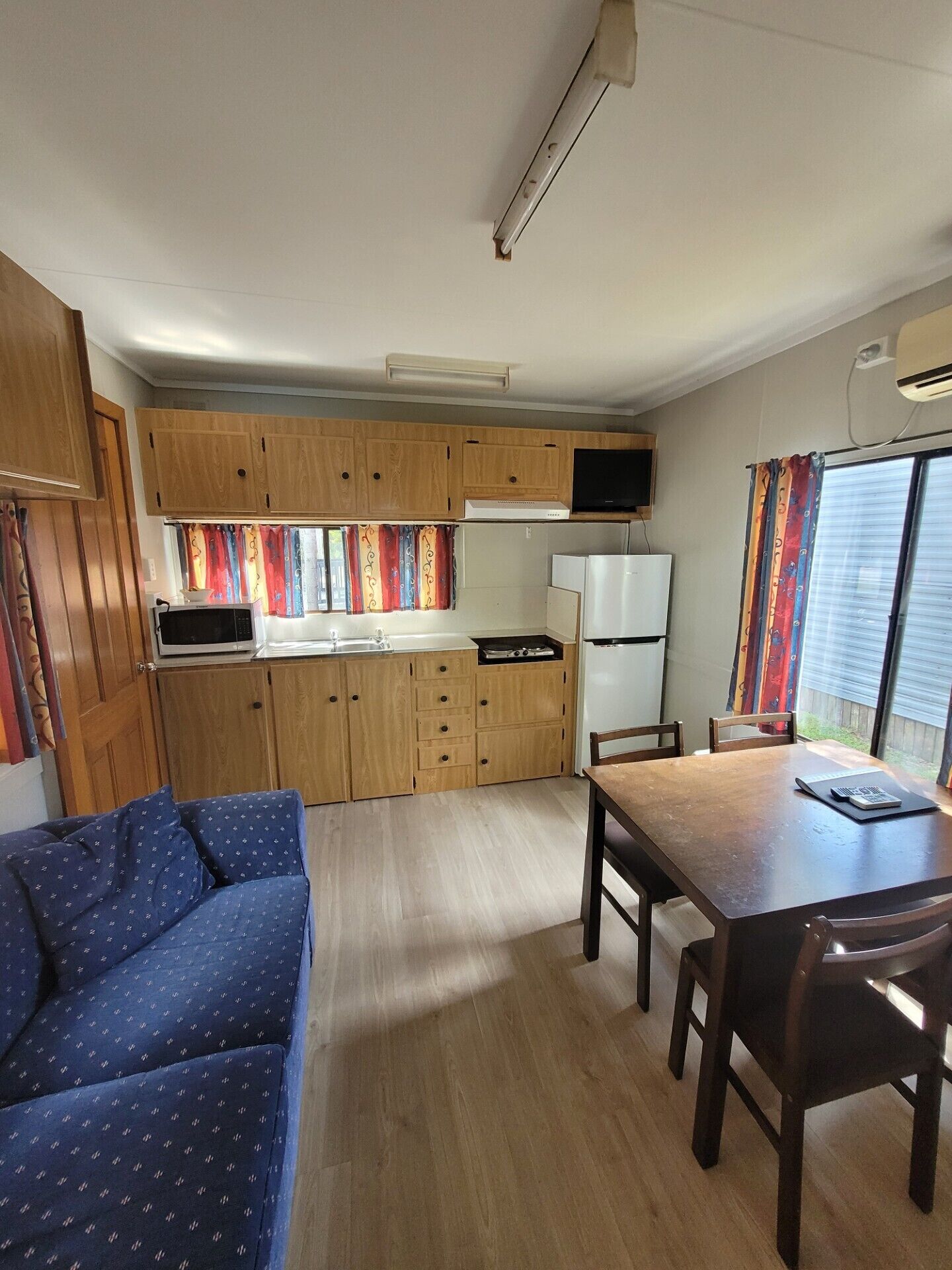 A compact kitchen with wooden cabinets, a microwave, a refrigerator, and a dining area with a table and chairs.
