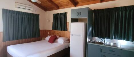 Une petite chambre comprenant un lit, un coin cuisine et un ventilateur de plafond.