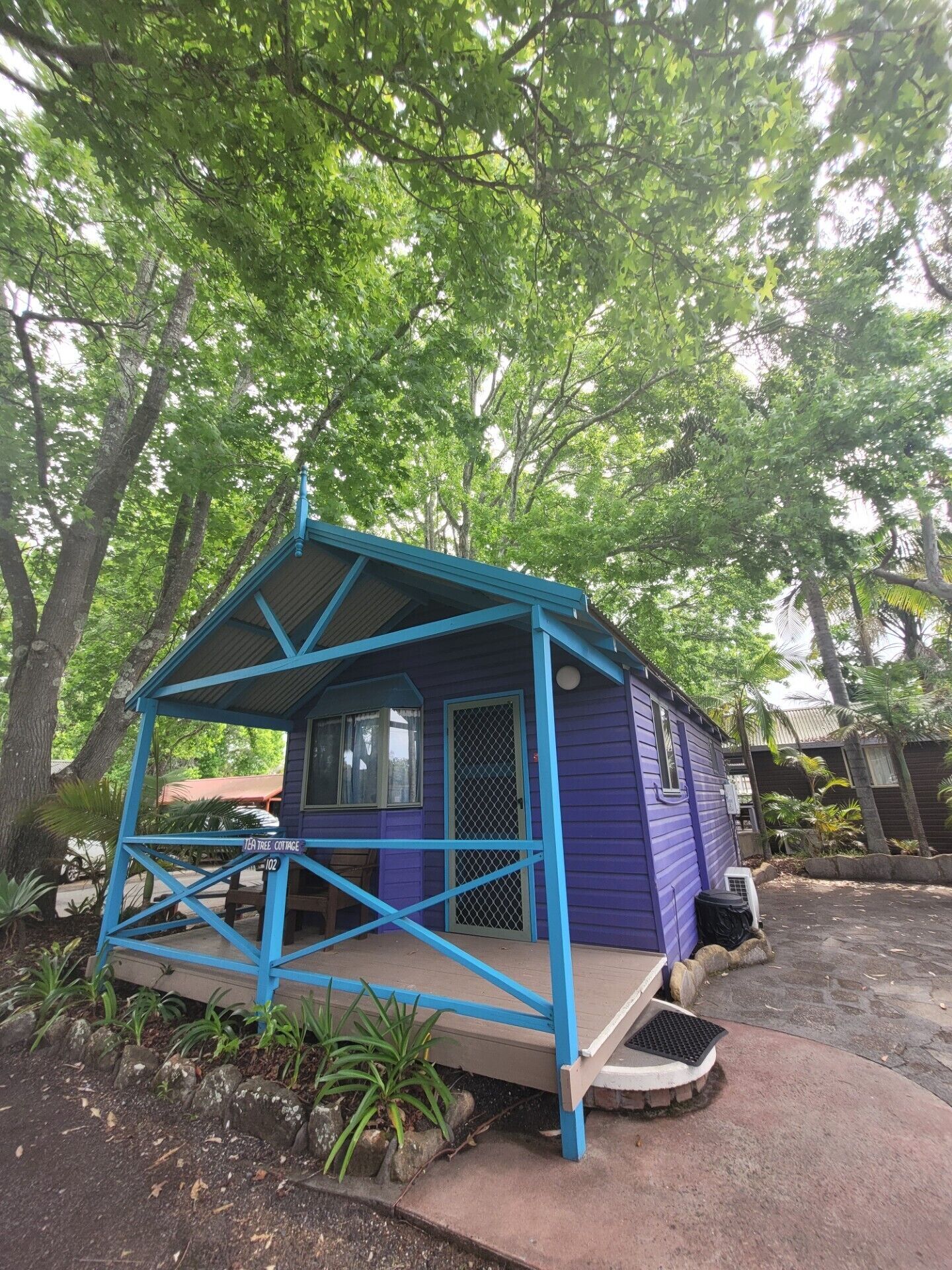 A small, single-story building with a blue roof and walls, surrounded by lush greenery.