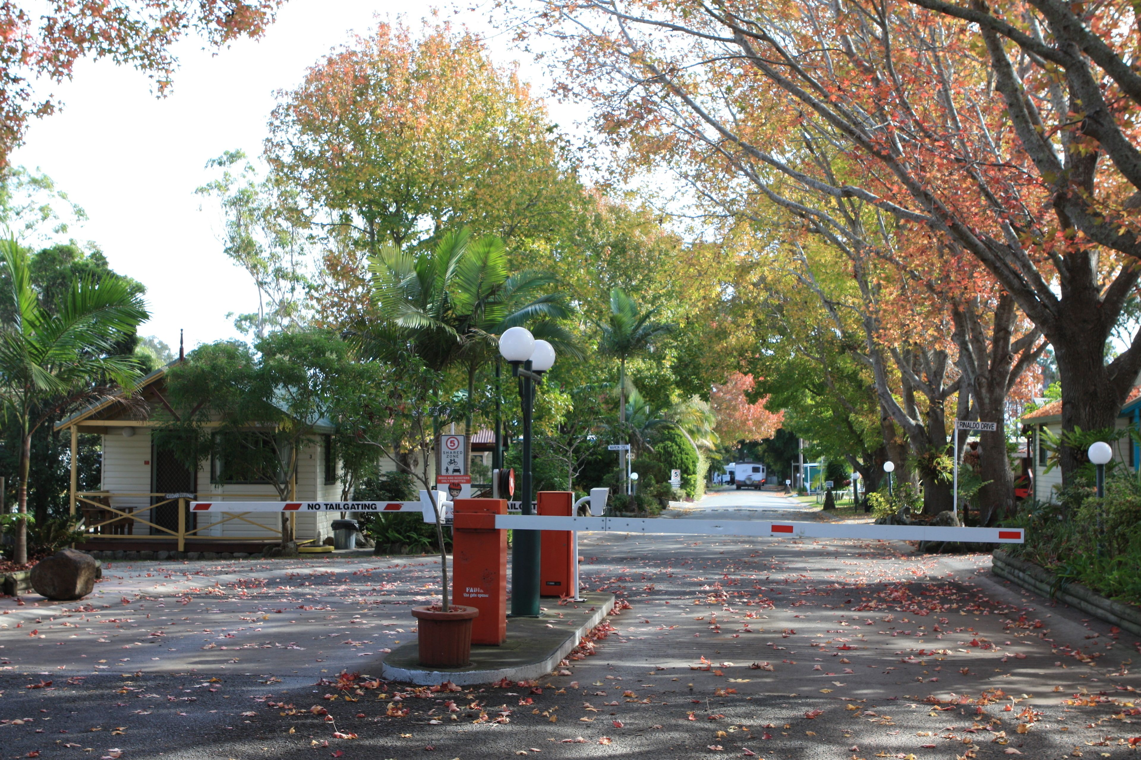 A gated entrance with a no tailgating sign, a small building, and trees with autumn leaves.