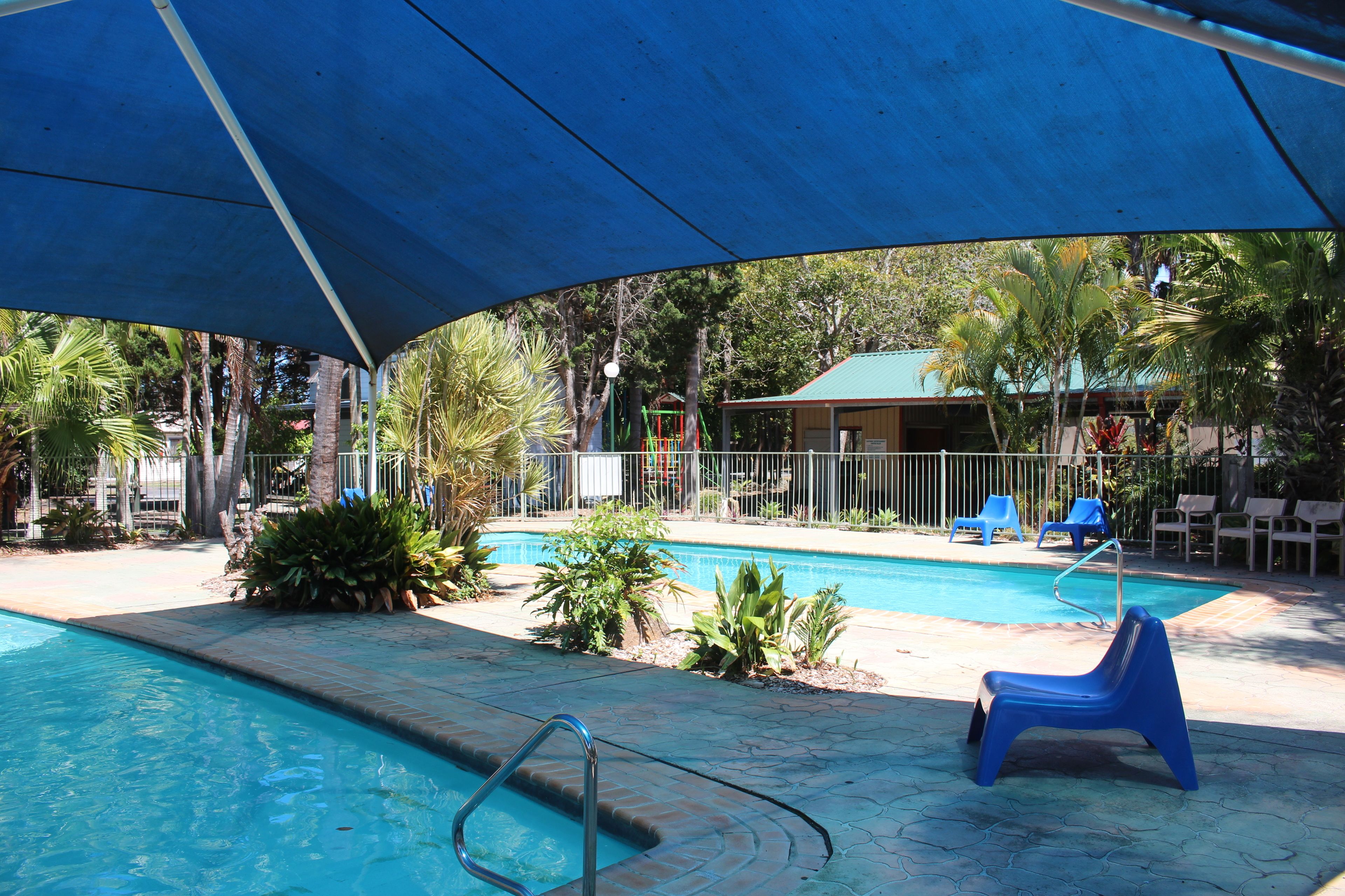 A swimming pool area with a covered section, lounge chairs, and a small building in the background.