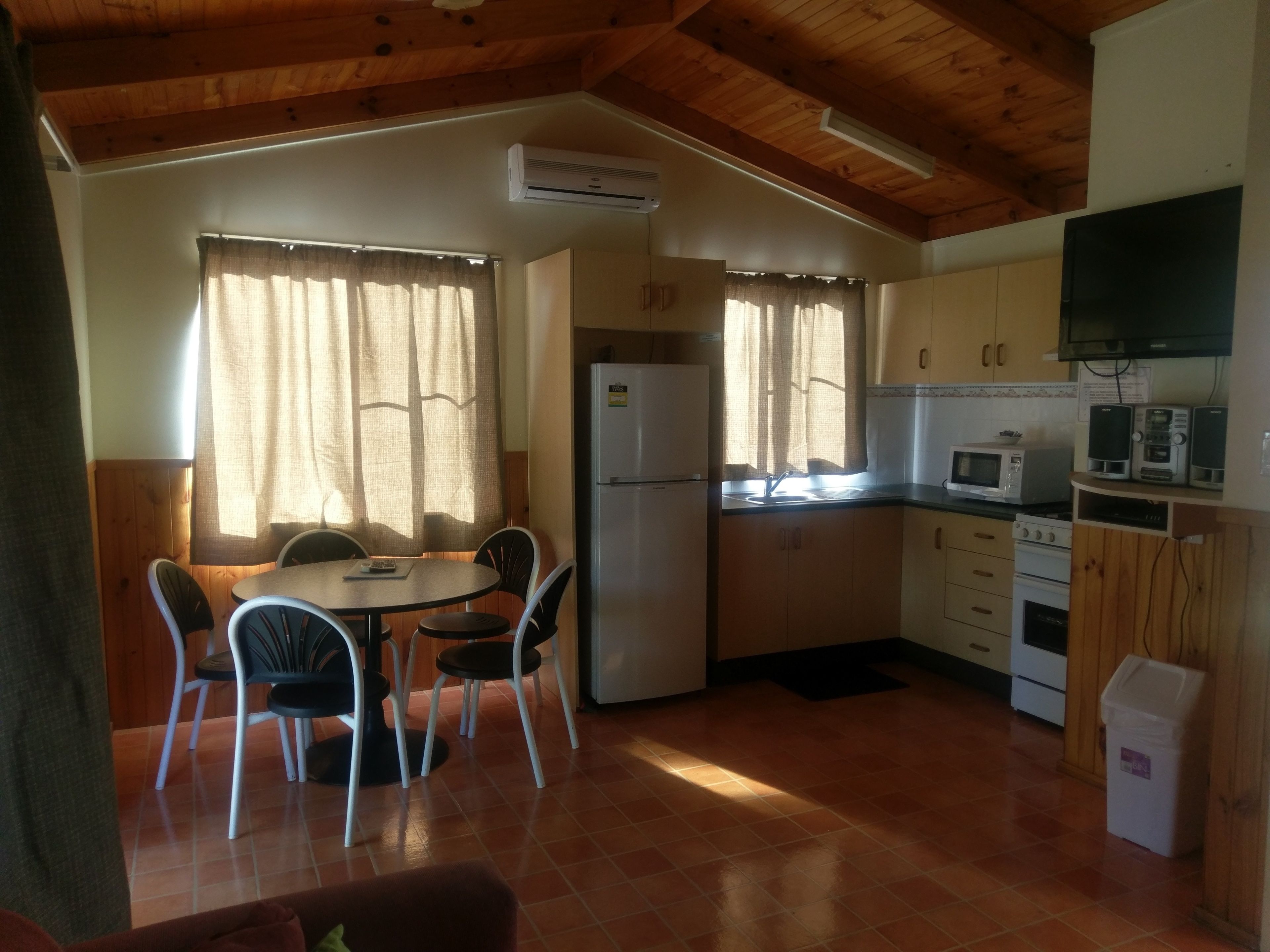 Cozinha compacta com geladeira, micro-ondas e fogão. Possui área de refeições com mesa e cadeiras.