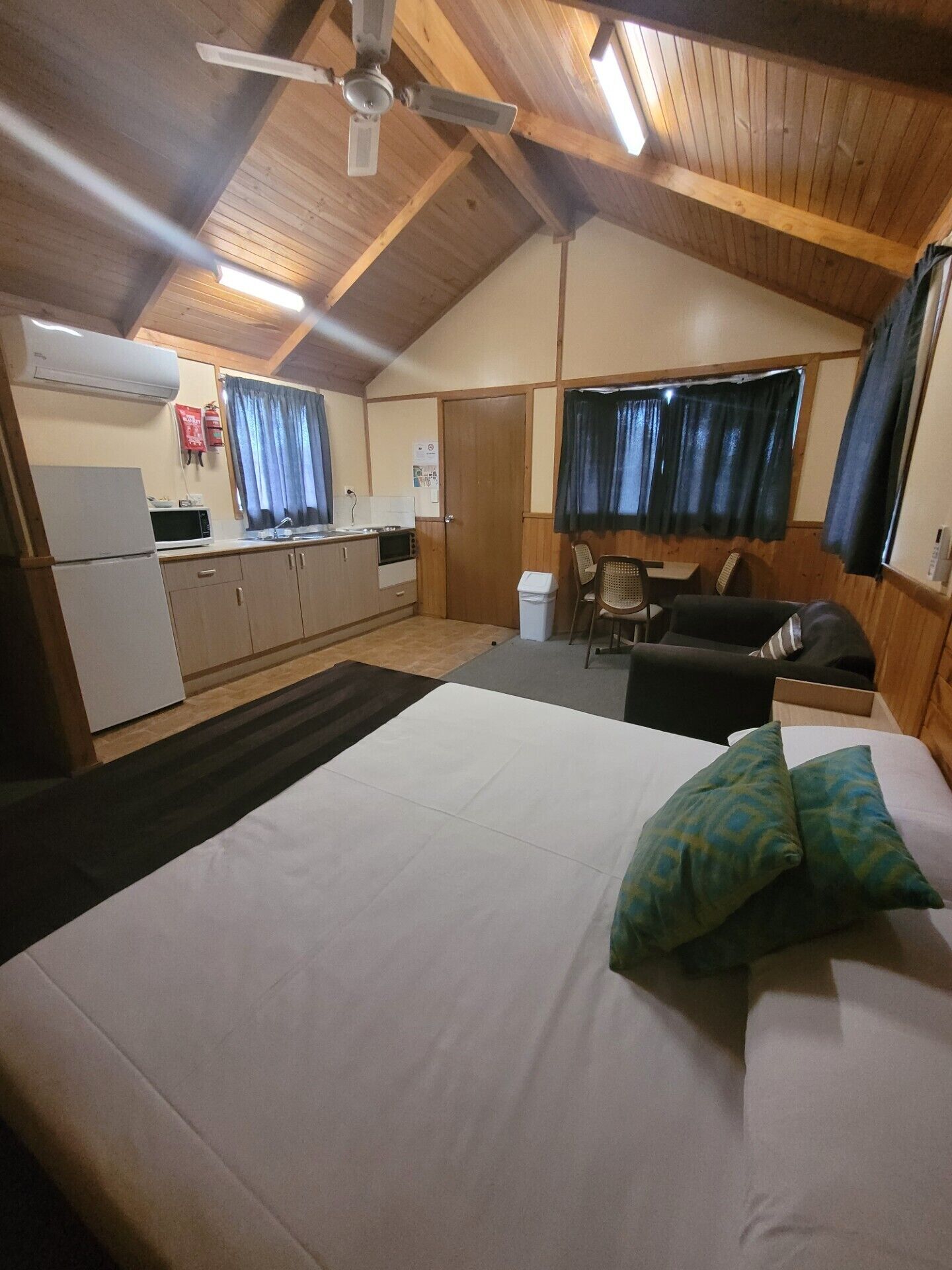 A room with a bed, a desk, a chair, a kitchenette, and a ceiling fan.