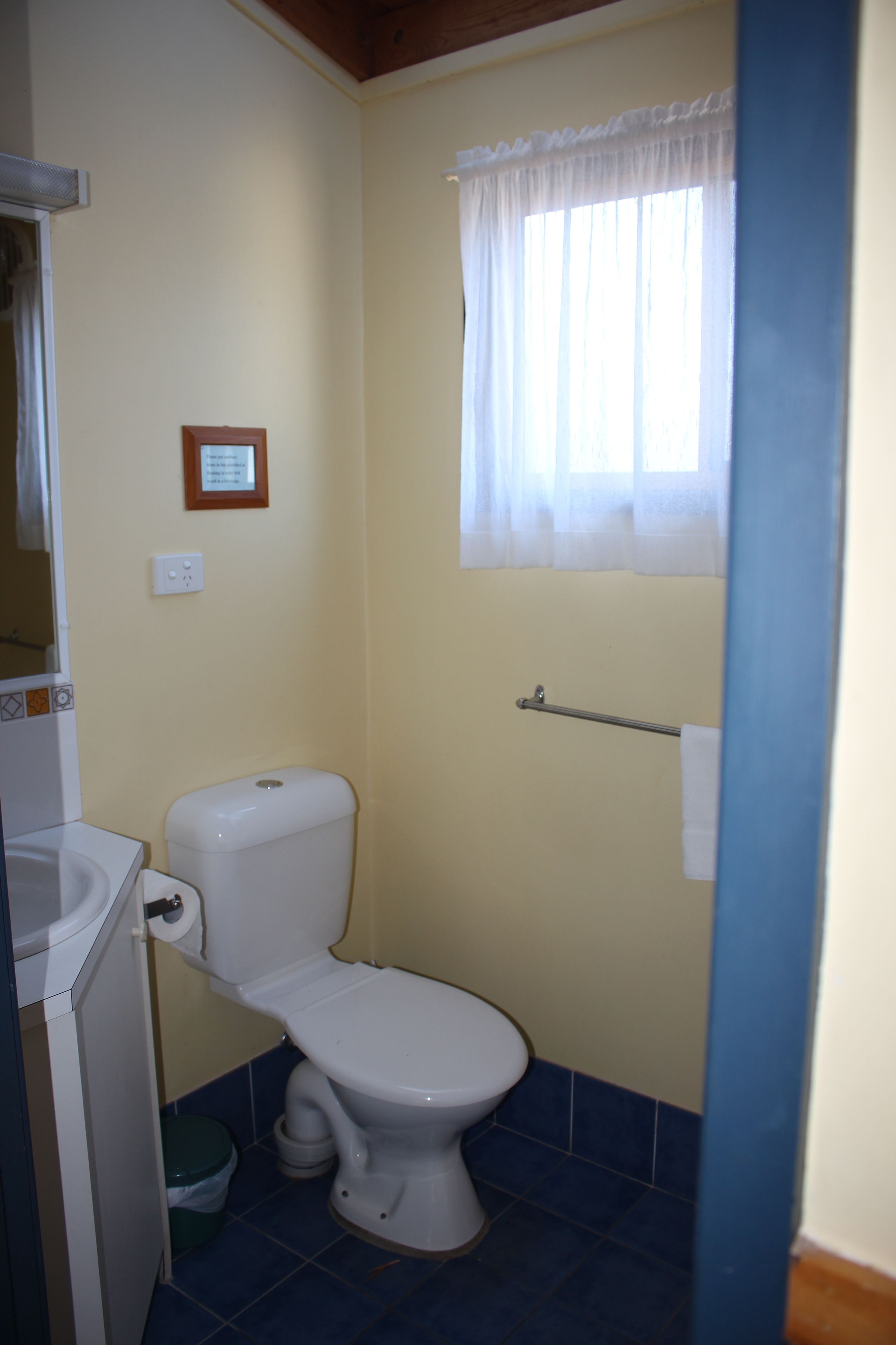 A small bathroom with a toilet, a sink, and a window with a curtain.