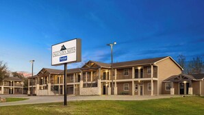 A hotel with a sign reading "Eagle's Den Suites" and "Travelodge". It features a multi-story building with balconies and a well-maintained lawn in front. - Eagle's Den Three Rivers Texas a Travelodge by Wyndham (Three Rivers)