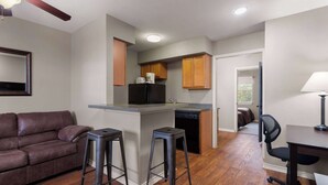 A compact living space with a kitchenette, a sofa, two bar stools, and a desk with a chair. - Eagle's Den Three Rivers Texas a Travelodge by Wyndham (Three Rivers)