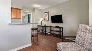 A compact living space with a kitchen area, a dining table, a bar stool, a television, and a patterned sofa. - Eagle's Den Three Rivers Texas a Travelodge by Wyndham (Three Rivers)