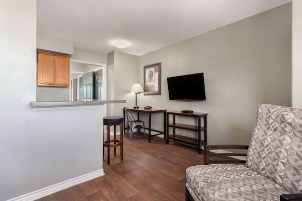 A compact living space with a kitchen area, a dining table, a bar stool, a television, and a patterned sofa.