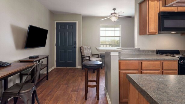 A compact kitchen with wooden cabinets, a built-in microwave, and a ceiling fan. - Eagle's Den Three Rivers Texas a Travelodge by Wyndham (Three Rivers)