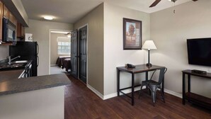 A modern kitchen with dark wood cabinets, a black refrigerator, and a granite countertop. There is a dining area with a table and chairs, a ceiling fan, and a mounted TV. - Eagle's Den Three Rivers Texas a Travelodge by Wyndham (Three Rivers)