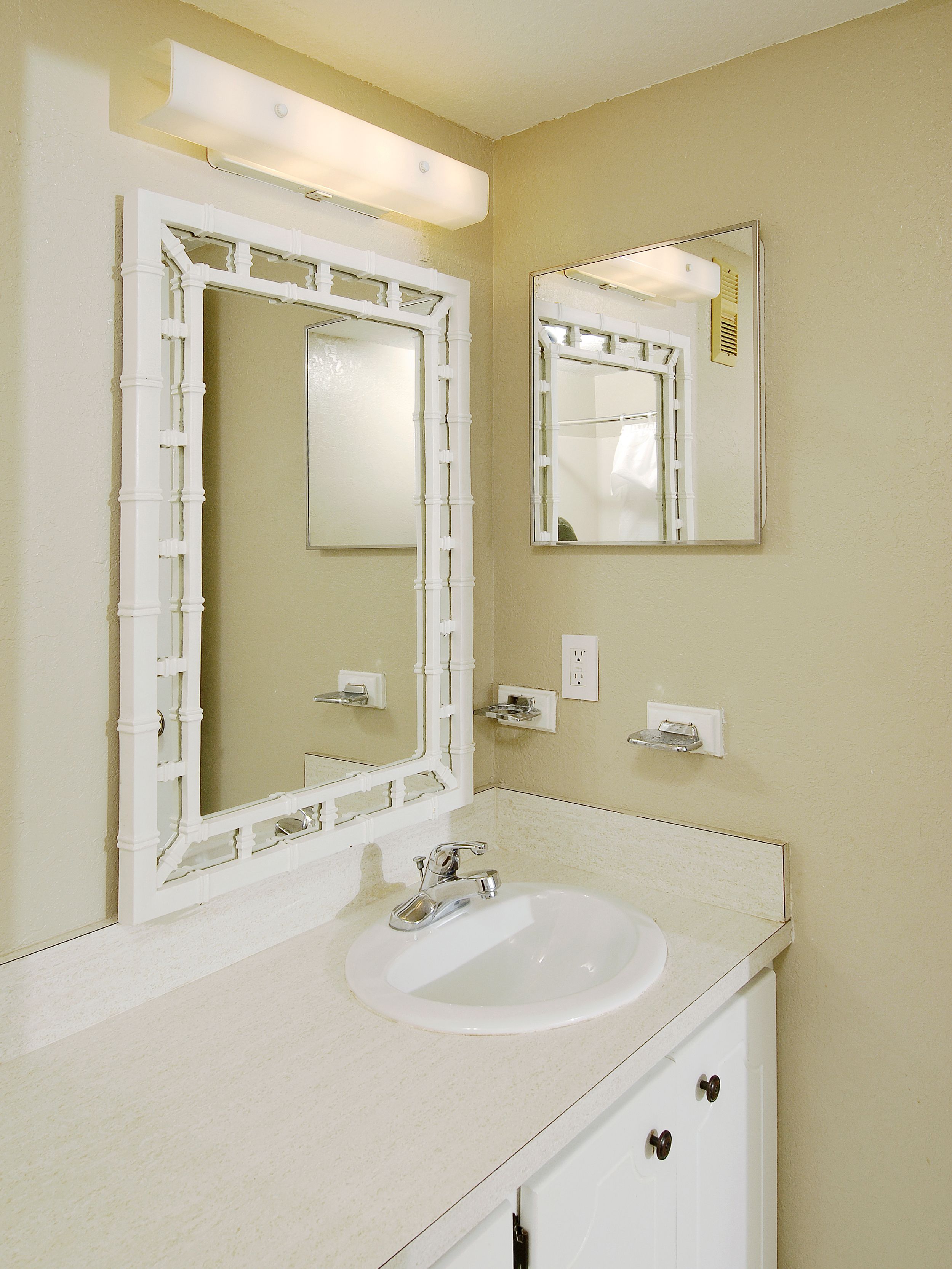 Une salle de bain avec un lavabo blanc, deux miroirs et un meuble-vasque.