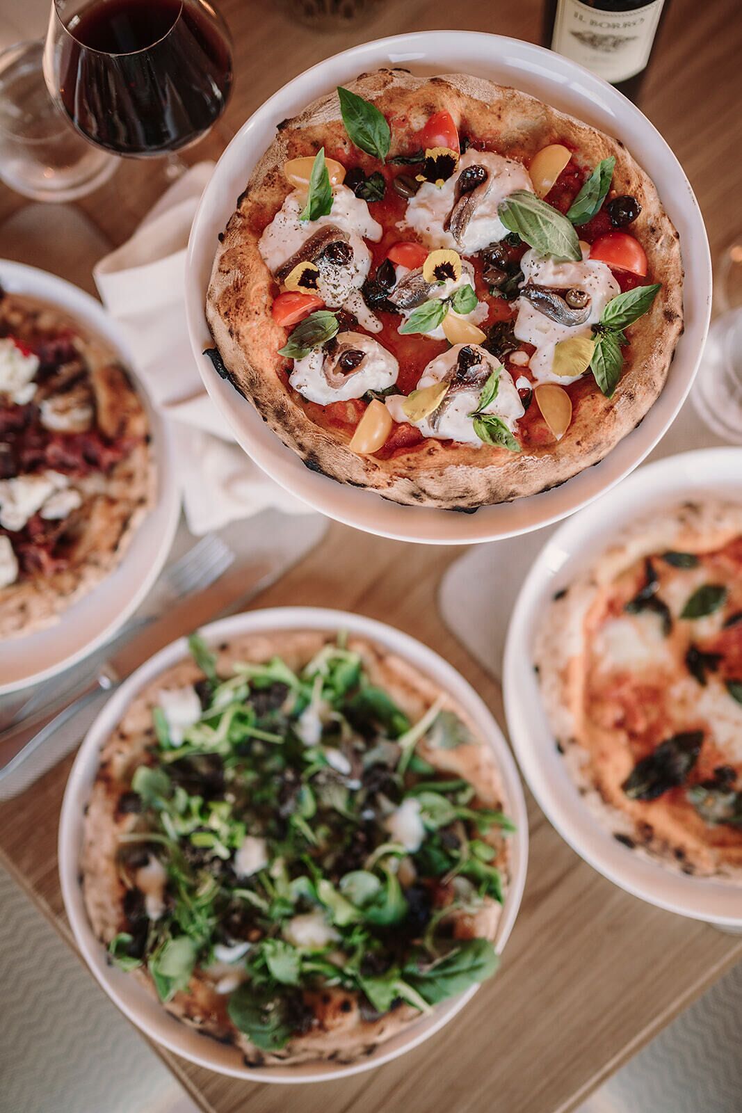 Verschiedene Pizzen auf einem Tisch, darunter eine mit Tomaten, Pilzen und Basilikum.