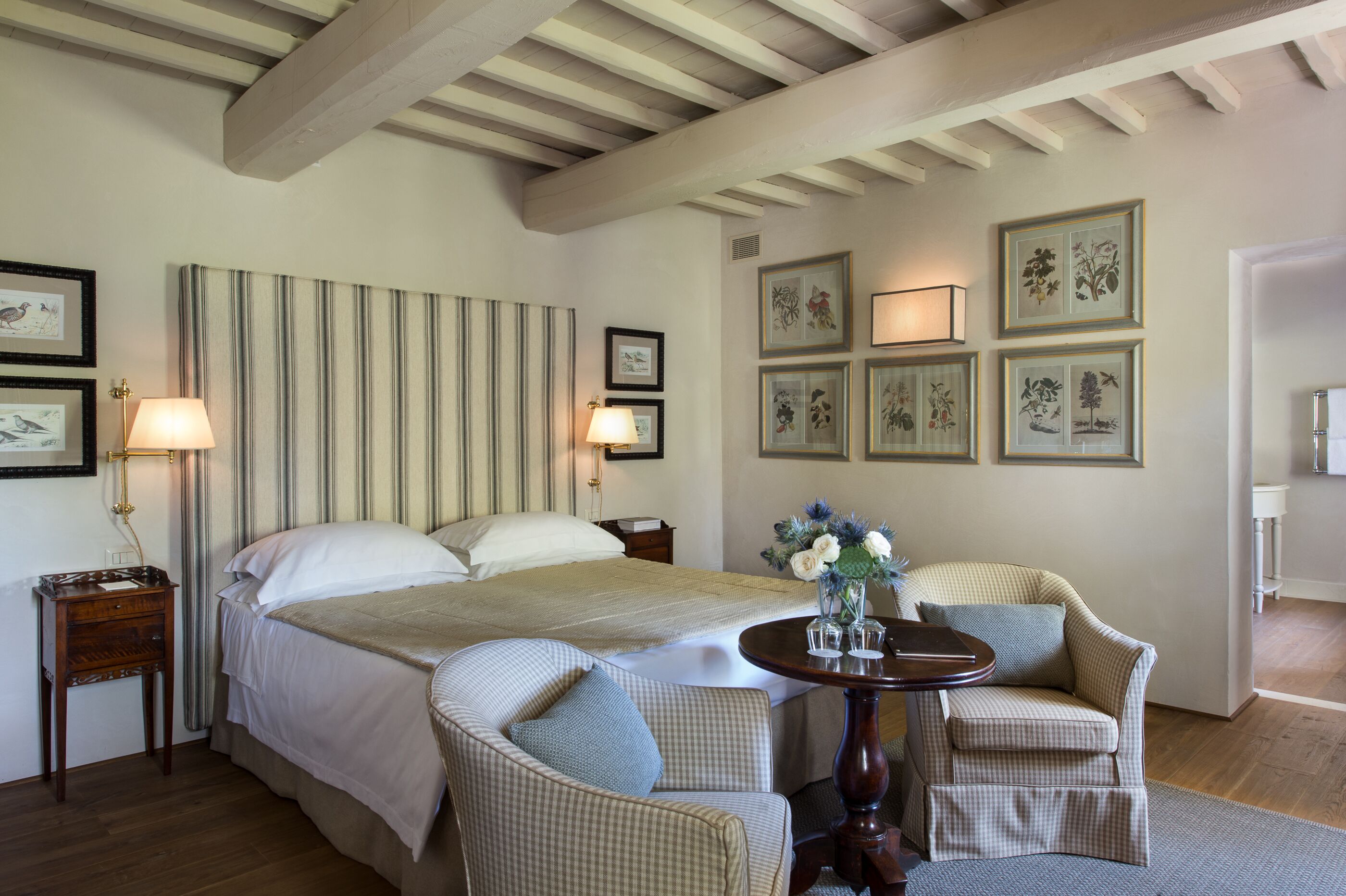 A hotel room with a large bed, two bedside tables, a small round table with chairs, and framed artwork on the walls.
