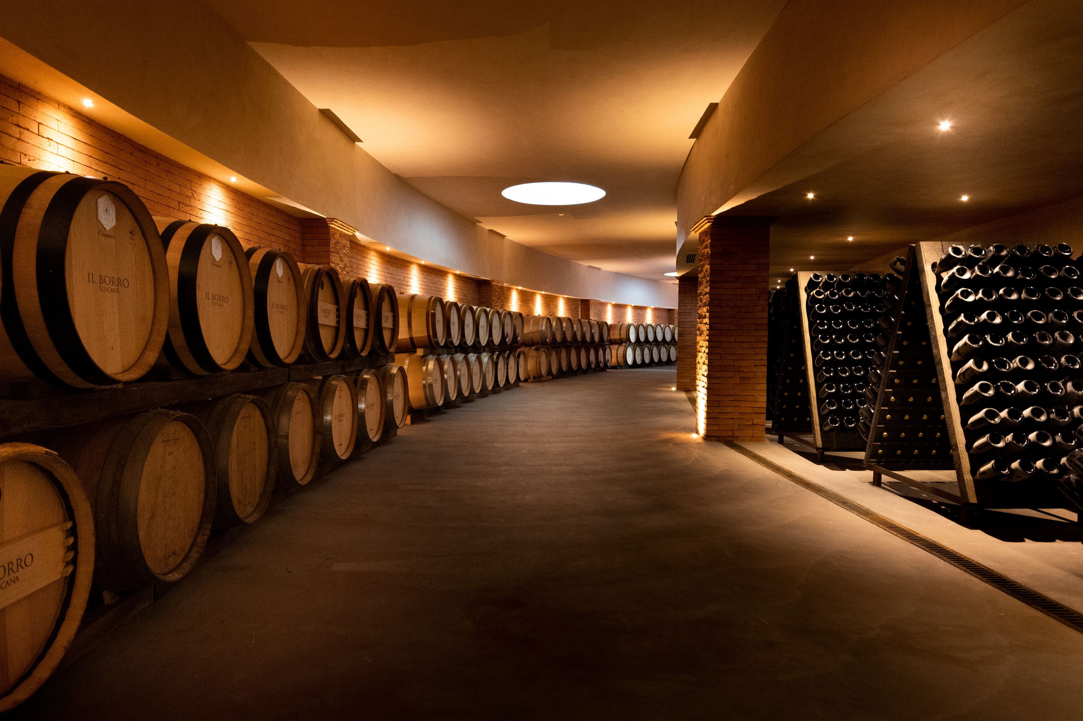 A wine cellar with rows of wooden barrels and a rack of wine bottles.