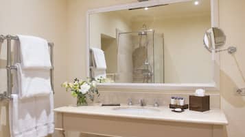A bathroom with a large mirror, two towel racks, a sink with toiletries, and a shower area.
