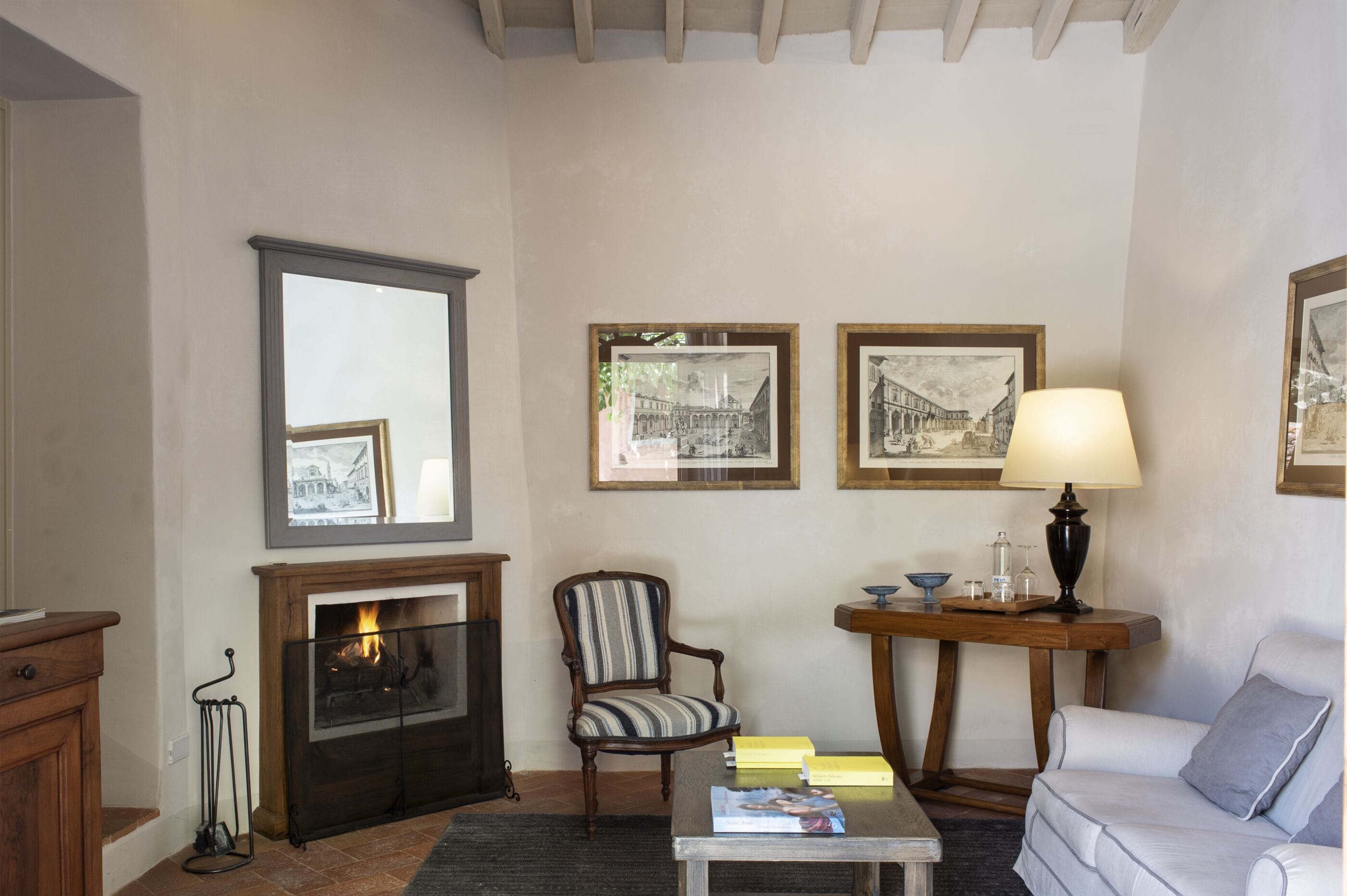 Un salon chaleureux avec une cheminée, des tableaux encadrés au mur, un fauteuil à rayures, une table d’appoint avec une lampe et un canapé.