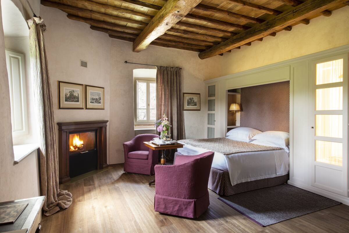Un dormitorio con chimenea, una cama, un escritorio con lámpara y dos sillones.