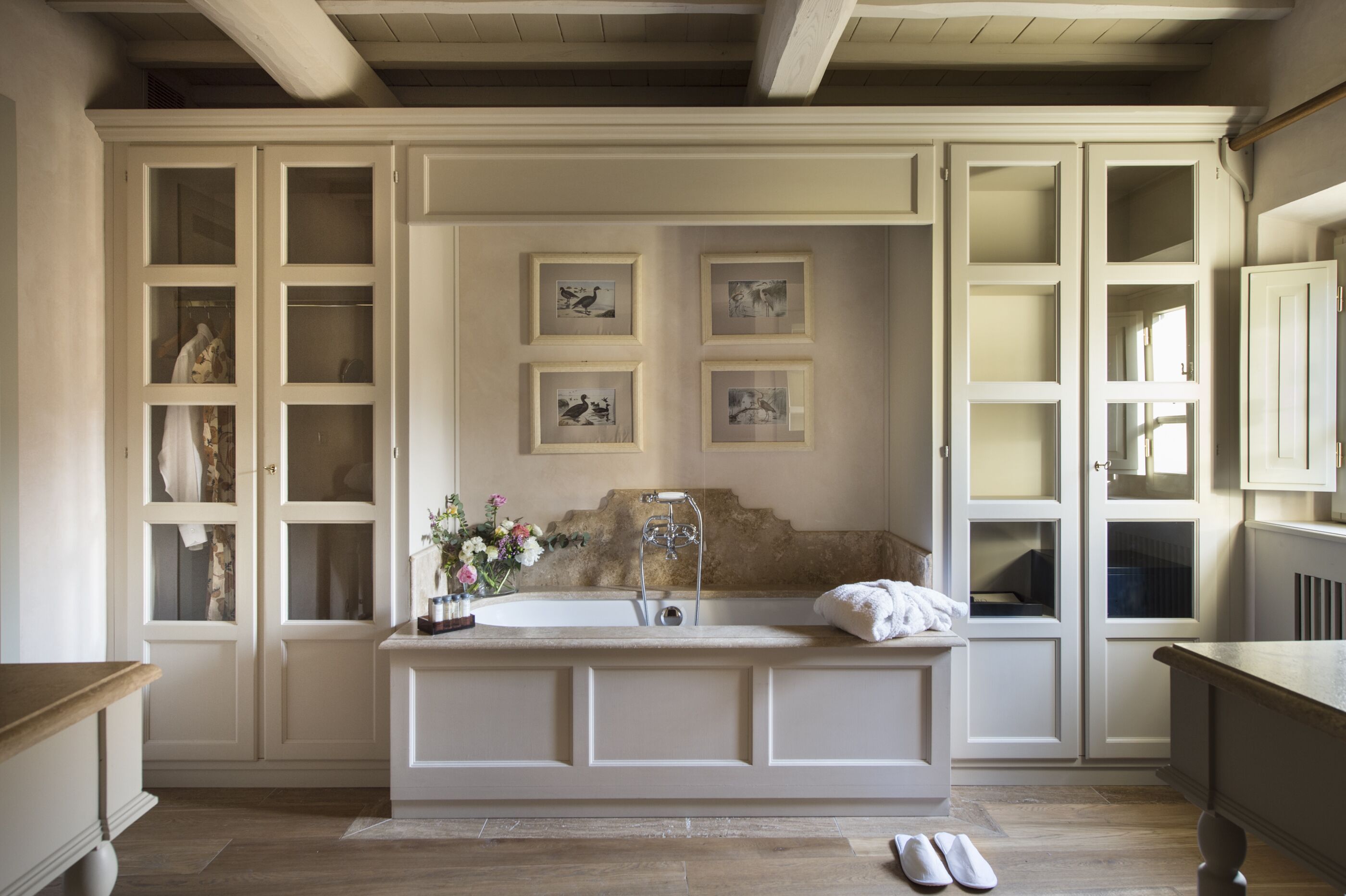 A bathroom with a freestanding bathtub, a vanity with a mirror, and a sink. There are framed pictures on the wall above the bathtub.