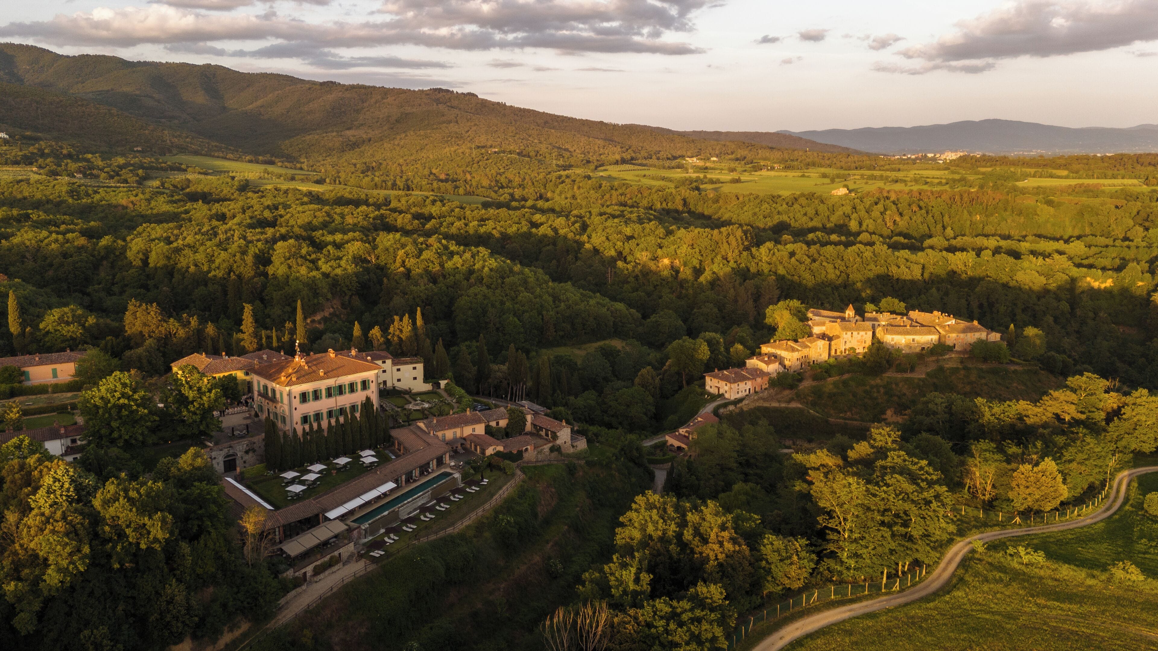 Vista aérea de una finca histórica con un amplio conjunto de edificios, rodeada de exuberante vegetación y colinas ondulantes.