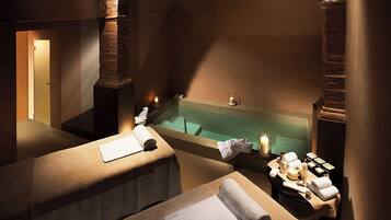 Relax in a serene spa room with a large arched fireplace, two massage tables, and a warm ambiance.