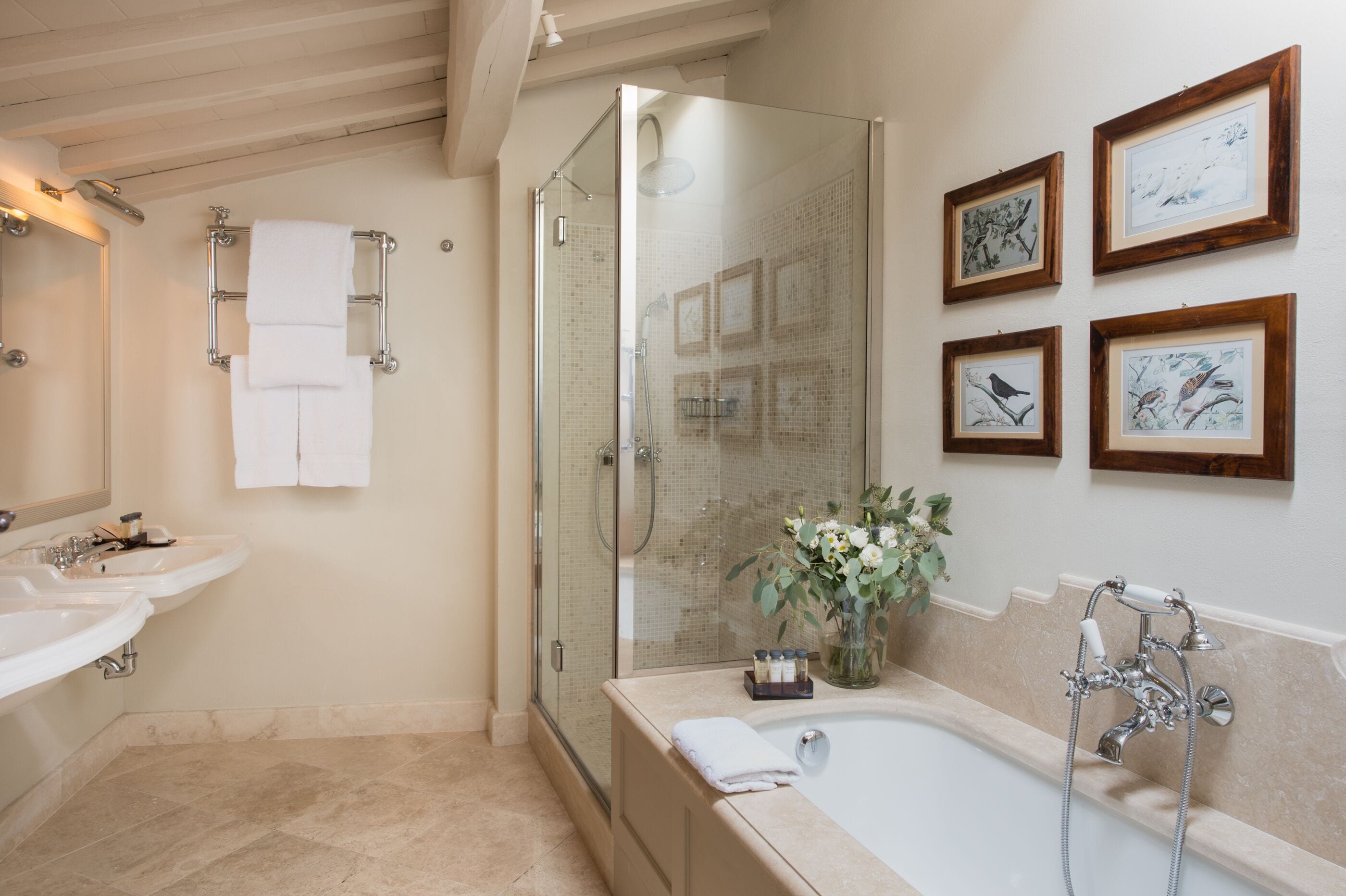 Un baño moderno con ducha envuelta en vidrio, dos lavamanos, una bañera y obras de arte enmarcadas en la pared.