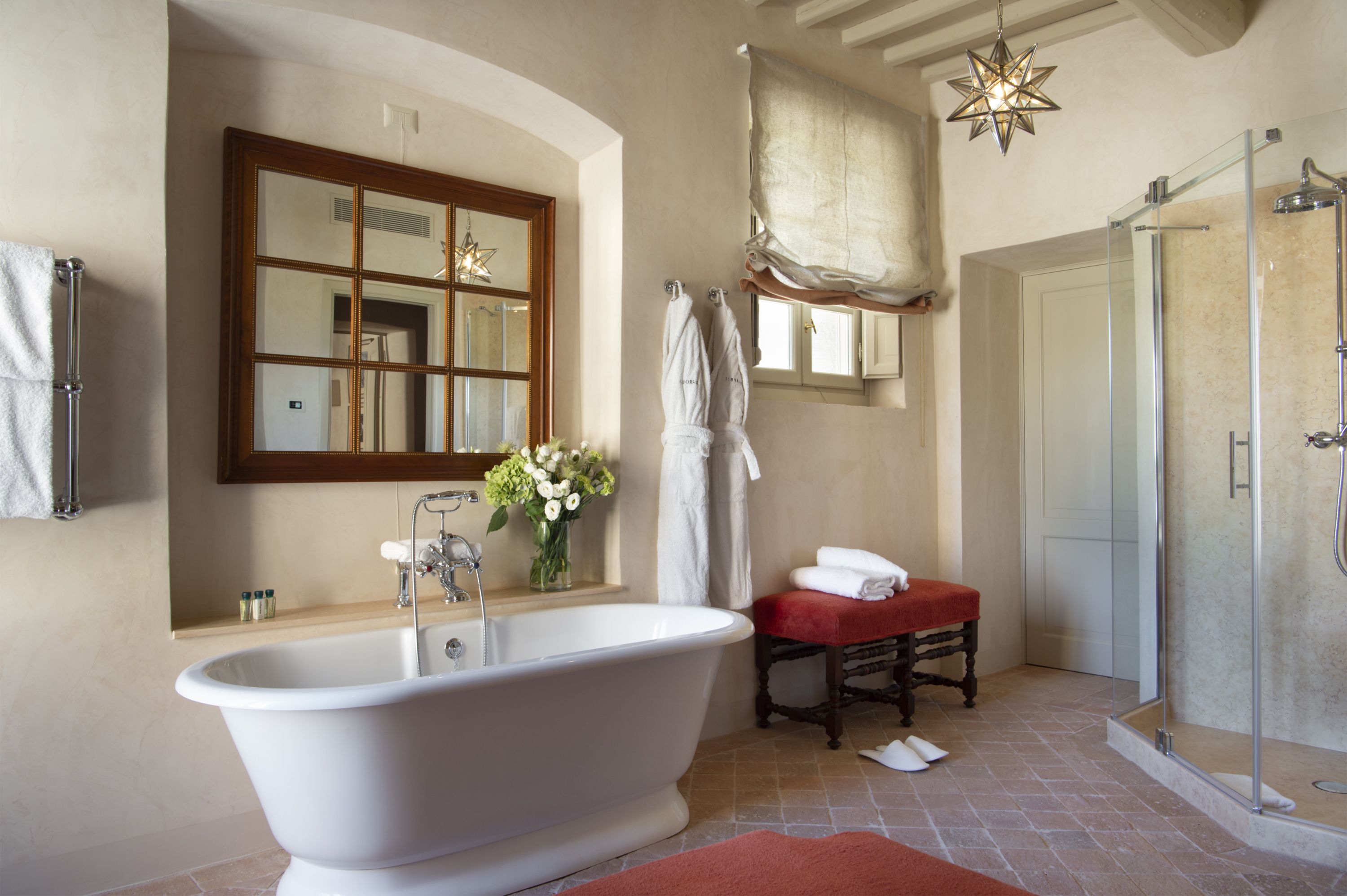 Une salle de bain avec une baignoire sur pieds, un espace de douche vitré, un meuble-lavabo avec un miroir et un banc rouge.