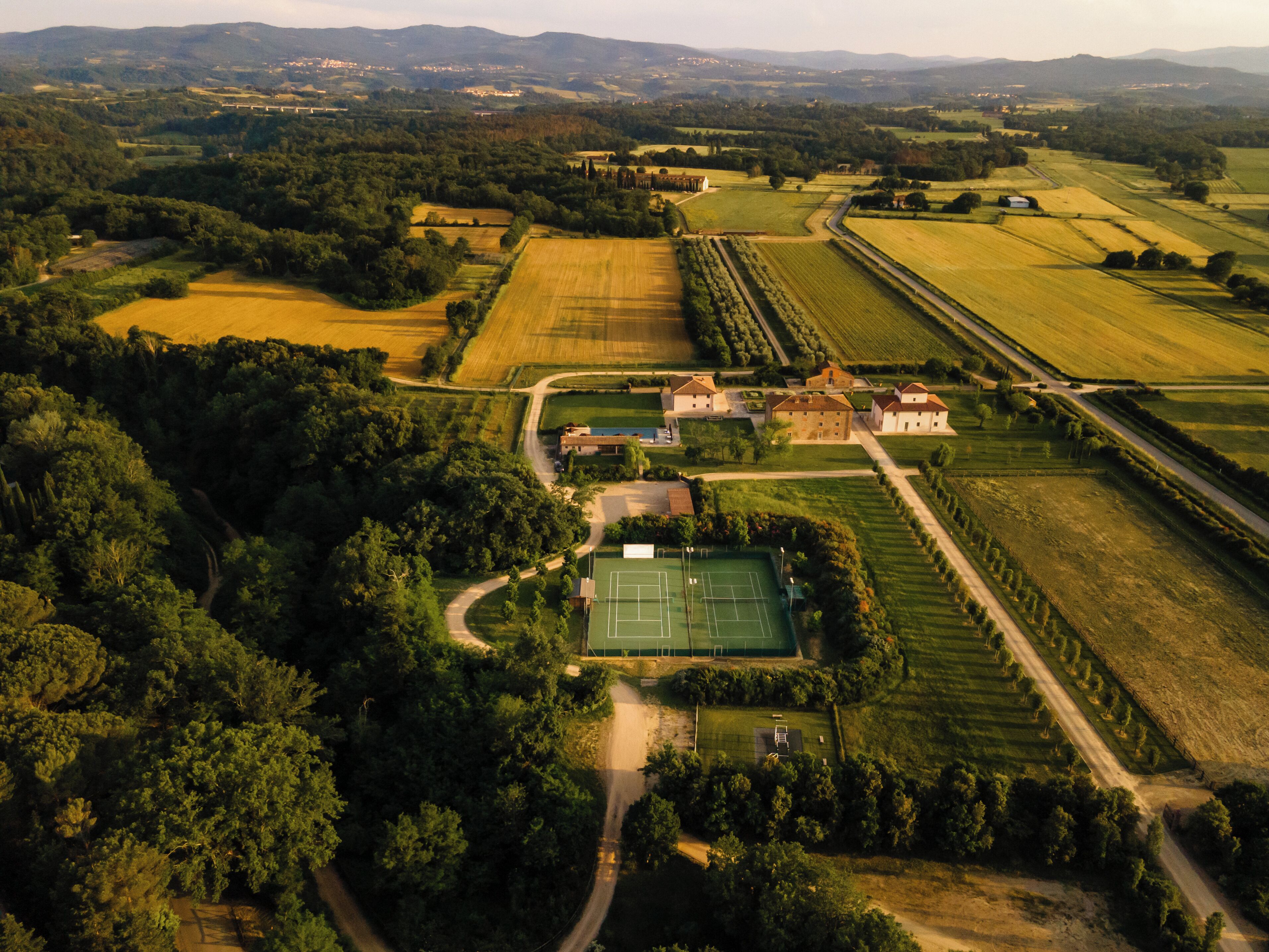 An aerial view of a rural estate with fields, a tennis court, and several buildings.