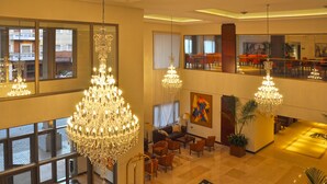 Un vestíbulo de hotel con candelabros, zonas de estar y vistas a la ciudad a través de amplias ventanas.