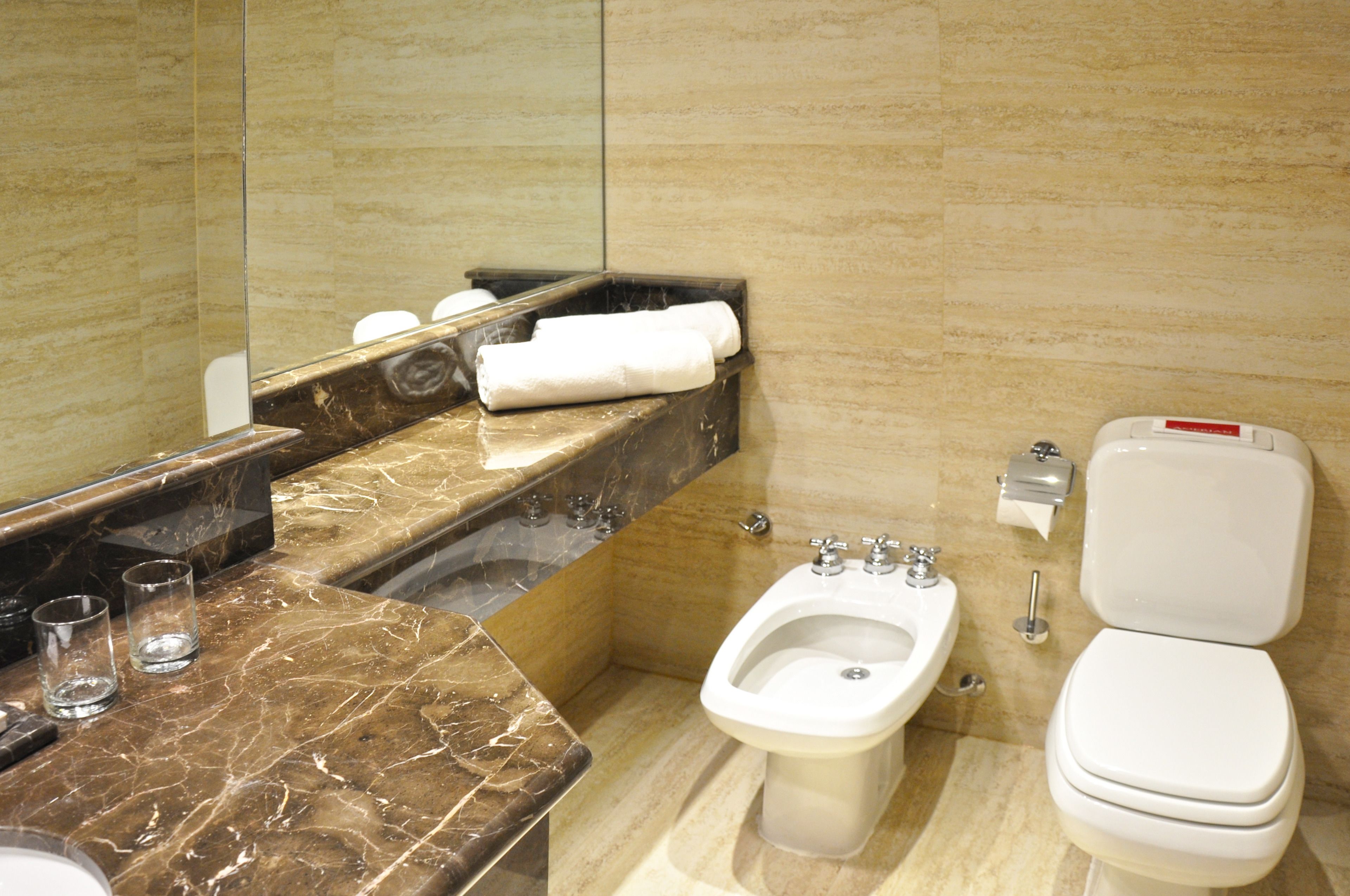 A bathroom with a marble vanity, a bidet, a toilet, and a mirror.