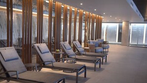 Un área interior moderna de relajación con sillones, mesas, ventanas amplias y un panel de pared de madera.