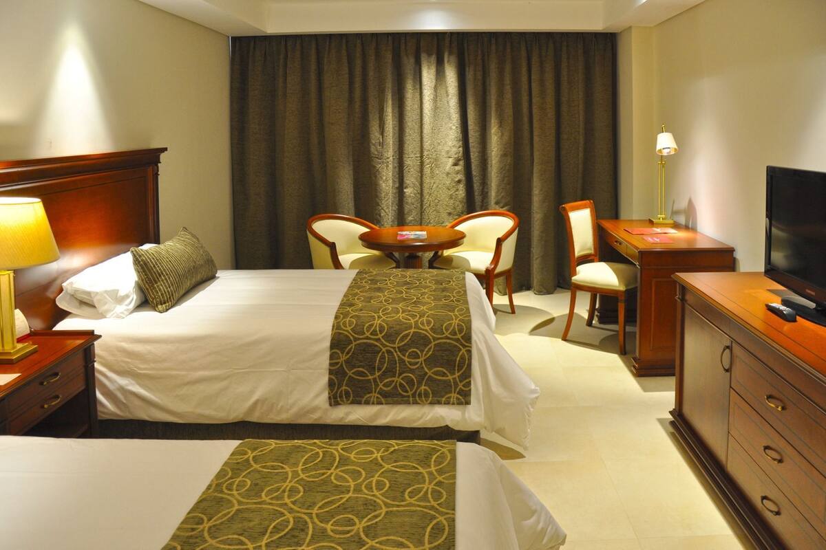A hotel room with a bed, two chairs, a desk, a television, and a lamp.