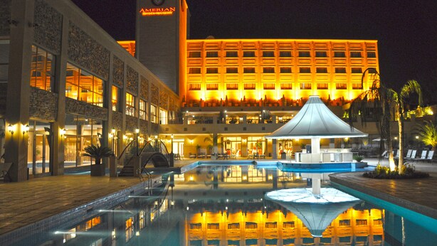 Un hotel con piscina, un espacio cubierto y un edificio grande con ventanas iluminadas.