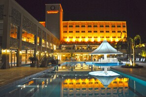 Un hotel amb piscina, zona coberta i un edifici gran amb finestres il·luminades.