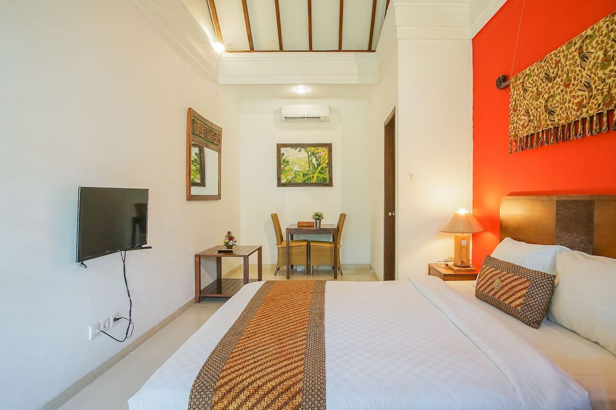 A hotel room with a bed, a TV, a dining table with chairs, a lamp, and a wall-mounted air conditioner.
