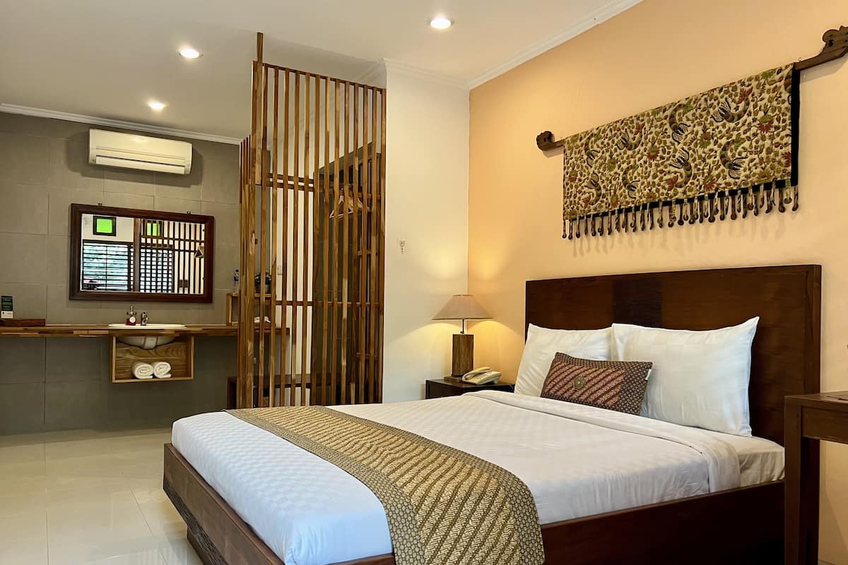 A neatly arranged bedroom with a wooden bed, a bedside table with a lamp, a wall-mounted air conditioner, and a decorative tapestry.