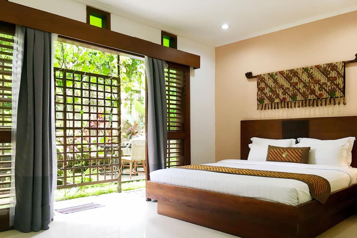 A bedroom with a large bed, a wooden headboard, and a view of greenery through a window with a wooden lattice.