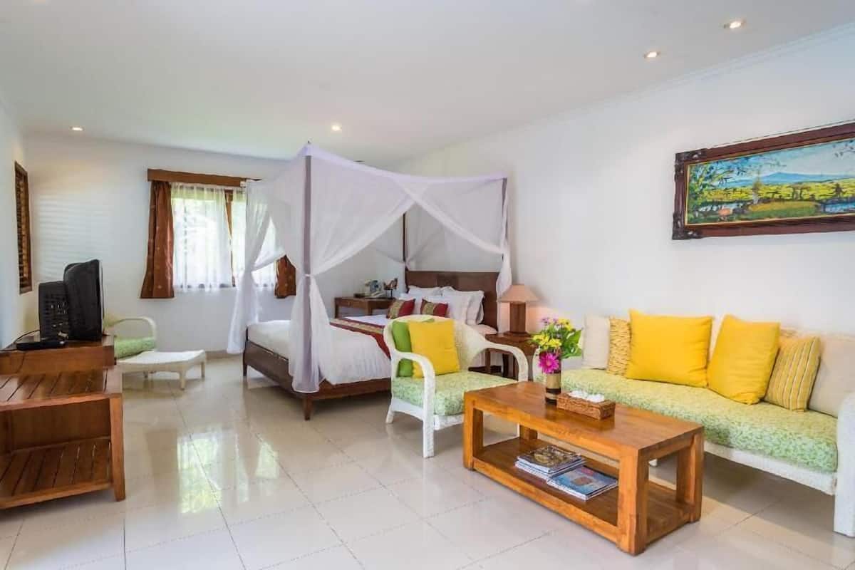 A bedroom with a four-poster bed, a sofa, a coffee table, and a painting on the wall.
