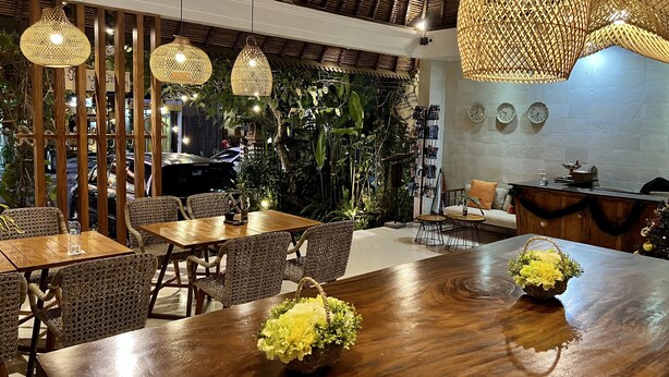 A restaurant with wooden tables and chairs, hanging wicker lamps, and a reception desk. - Villa Puriartha Ubud (Ubud)