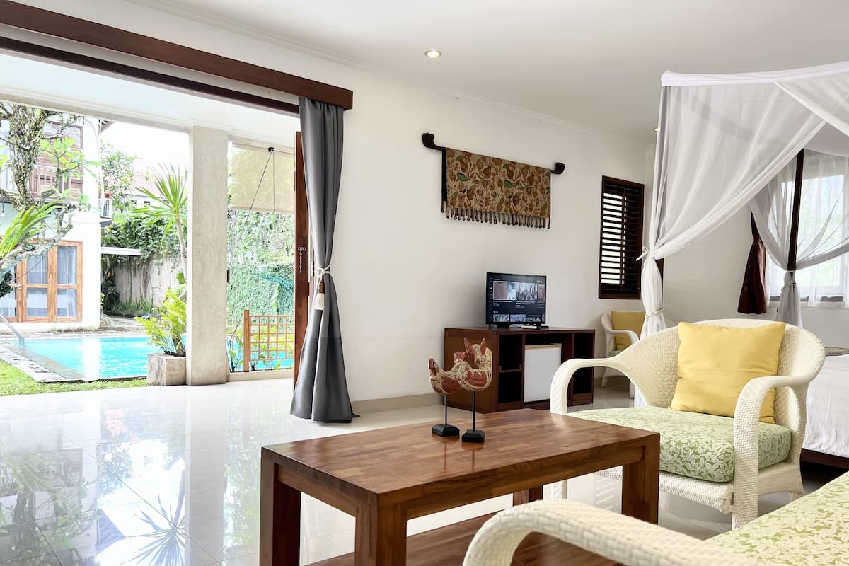 A spacious living area with a wooden coffee table, a white sofa with a yellow pillow, and a television on a wooden stand.