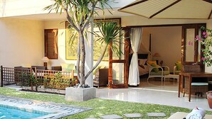 A pool area with a lounge chair, a small palm tree, and a dining area with chairs and a table. - Villa Puriartha Ubud (Ubud)