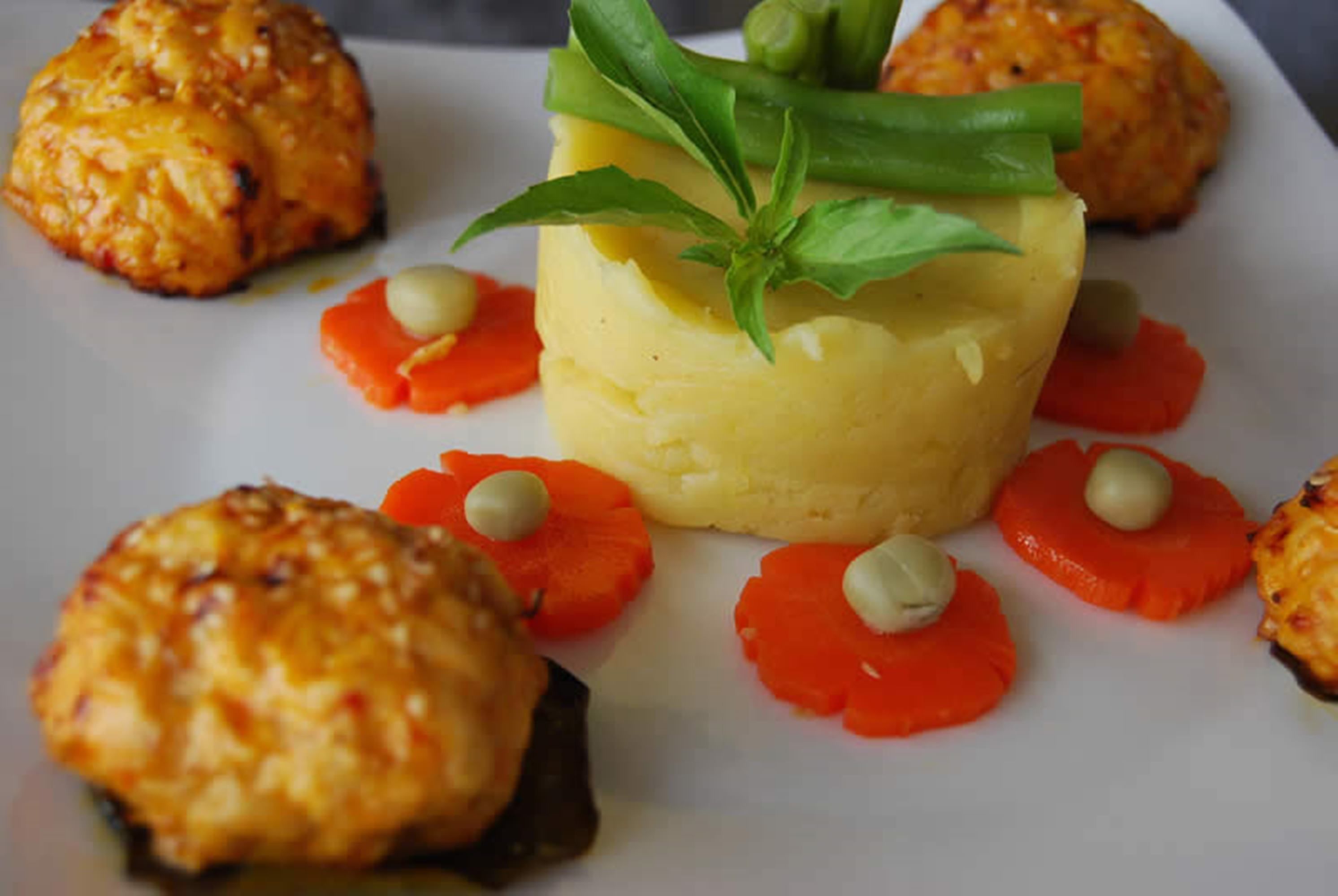 Um prato de purê de batatas, decorado com folhas verdes, cercado por fatias de cenoura e pequenas porções de creme.