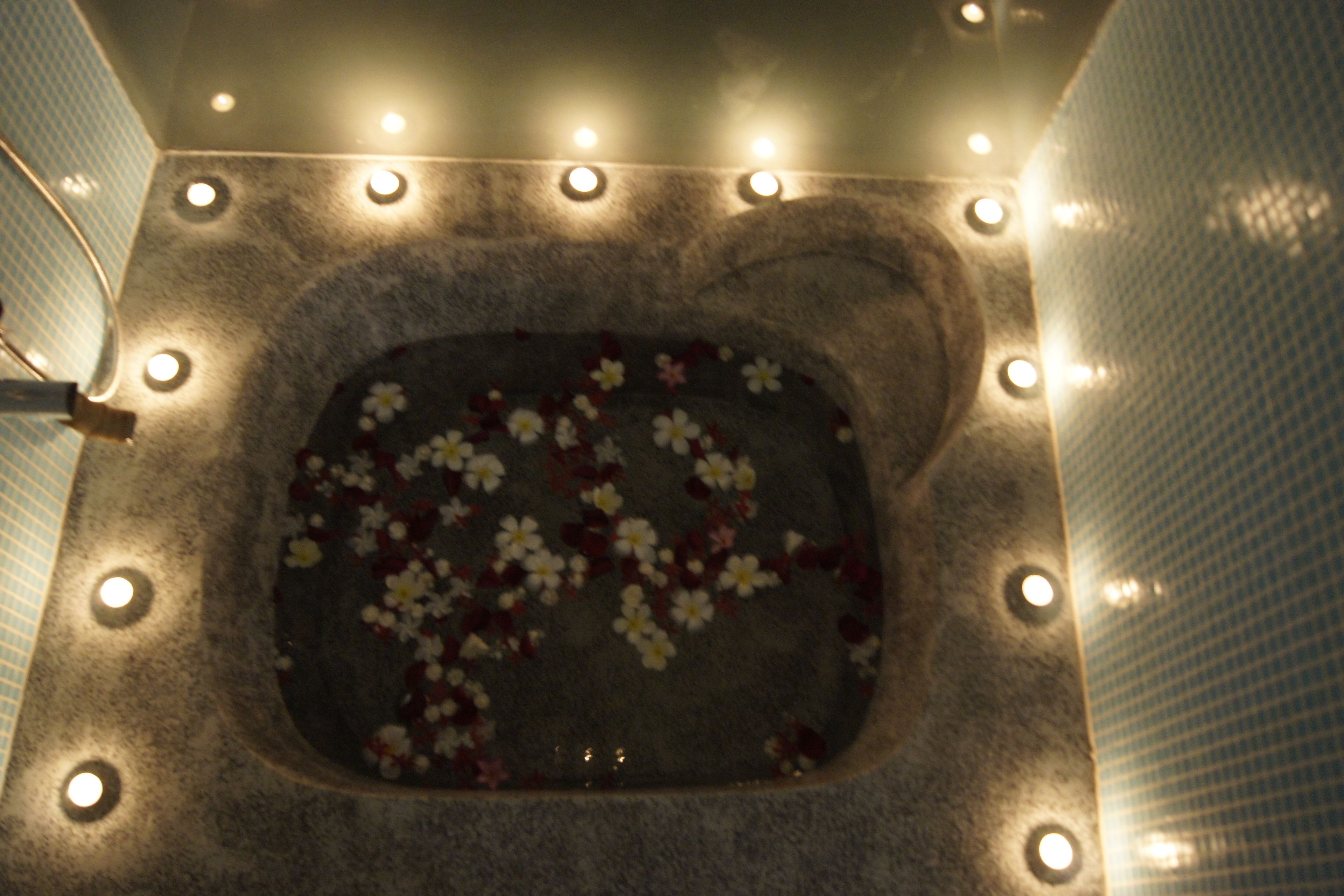 A square-shaped hot tub with a floral arrangement on the water's surface, surrounded by a series of lights.