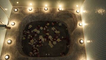 A square-shaped hot tub with a floral arrangement on the water's surface, surrounded by a series of lights.