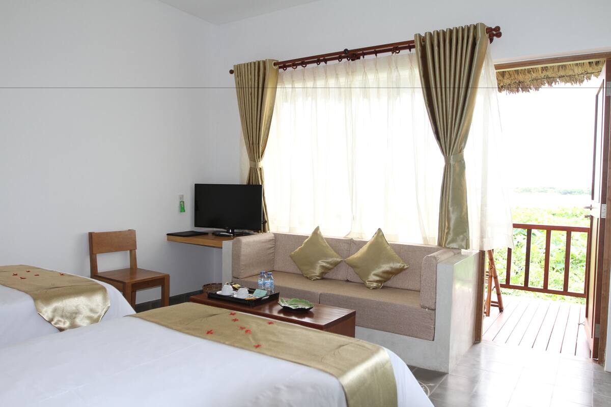 Una habitación de hotel con cama, sofá, televisión, escritorio y balcón.