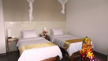 A hotel room with two beds, a bedside table with a vase of flowers, and a nightstand with a lamp.