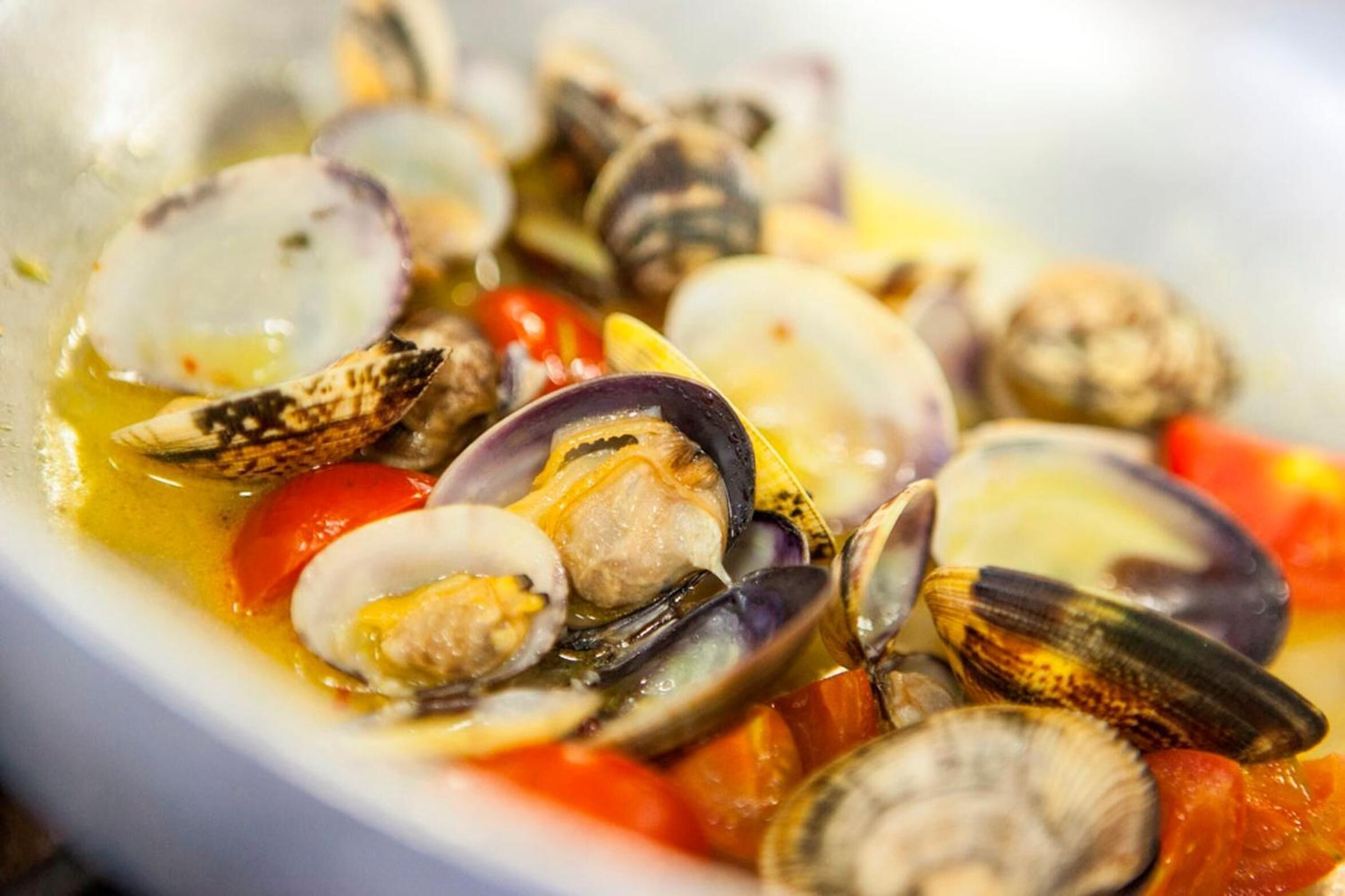 A bowl of seafood with clams and tomatoes.